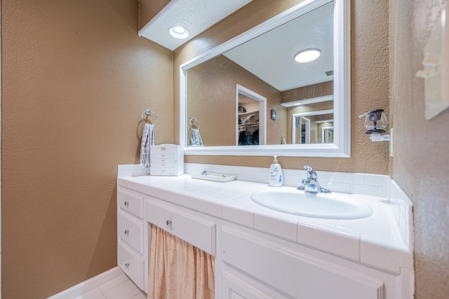 bathroom featuring vanity, a textured wall, tile patterned floors, and a spacious closet