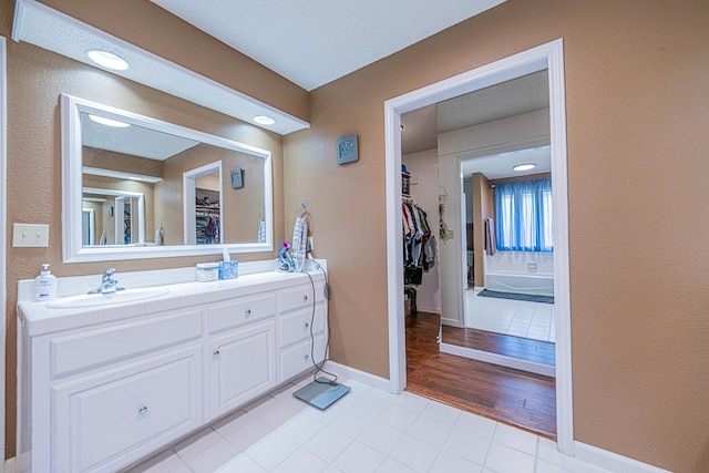 bathroom with a walk in closet, tile patterned flooring, double vanity, and baseboards