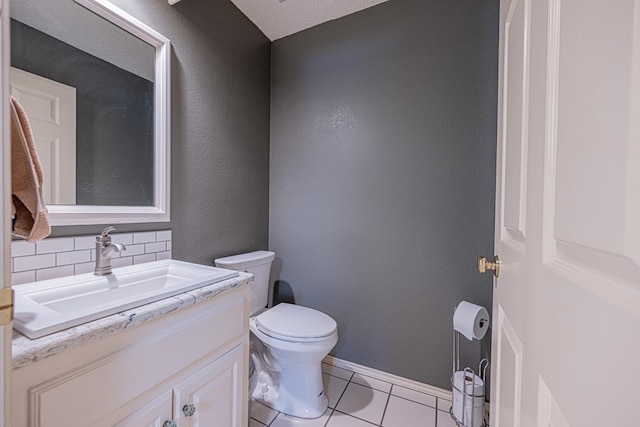 bathroom featuring toilet, tile patterned floors, vanity, tasteful backsplash, and a textured wall