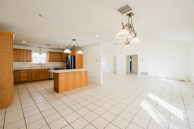 kitchen featuring dishwasher, black fridge, sink, hanging light fixtures, and a kitchen island