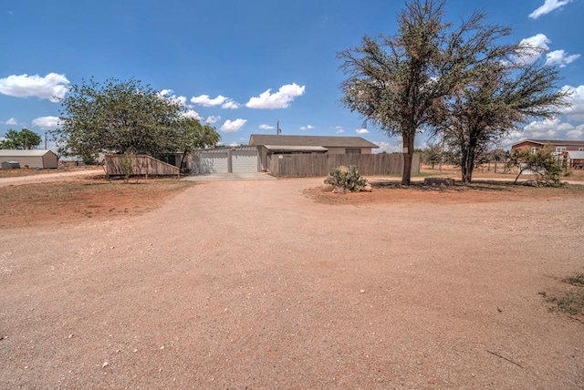 view of front of home with fence, a detached garage, a gate, dirt driveway, and a carport