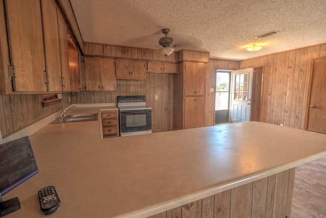 kitchen with electric range, a sink, light countertops, wood walls, and a peninsula