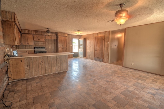 kitchen featuring electric range oven, brown cabinets, wood walls, light countertops, and a peninsula