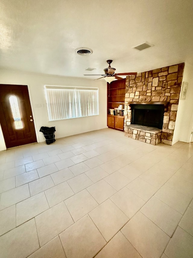 unfurnished living room with a fireplace, built in shelves, ceiling fan, and light tile patterned floors