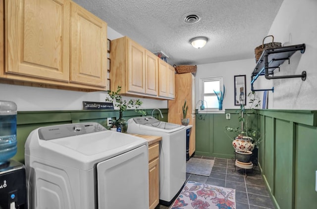 washroom featuring visible vents, dark tile patterned floors, washer and clothes dryer, cabinet space, and wainscoting