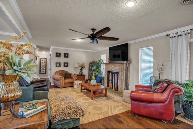 living area featuring a fireplace with raised hearth, ceiling fan, ornamental molding, wood finished floors, and a textured ceiling