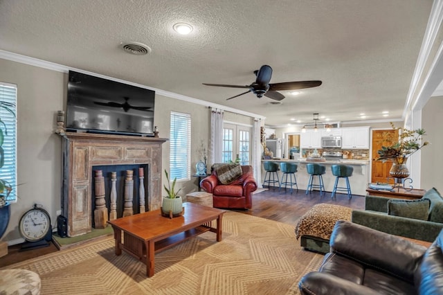 living area with visible vents, wood finished floors, a fireplace with raised hearth, and crown molding