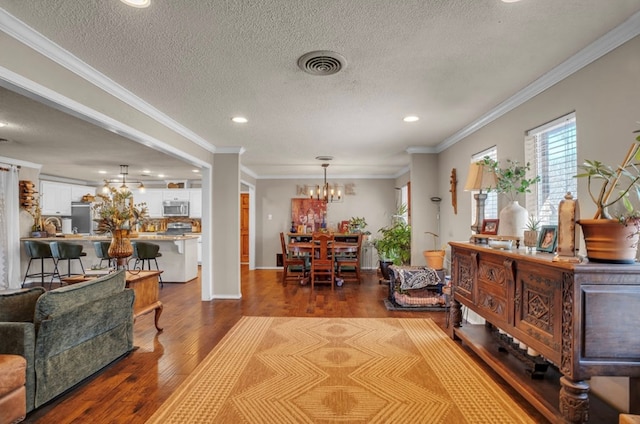 interior space with visible vents, a notable chandelier, a textured ceiling, wood finished floors, and crown molding