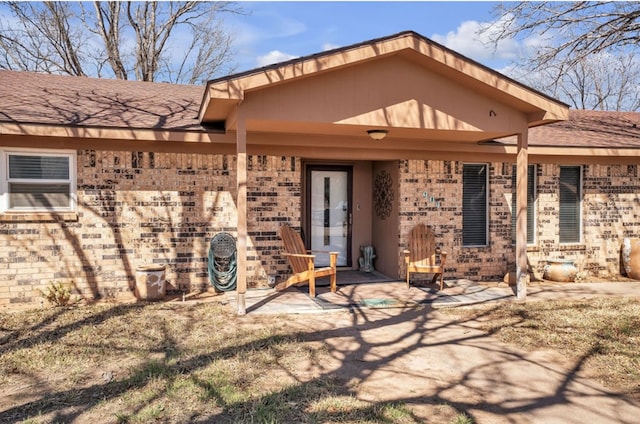 rear view of property with brick siding, a shingled roof, and a patio