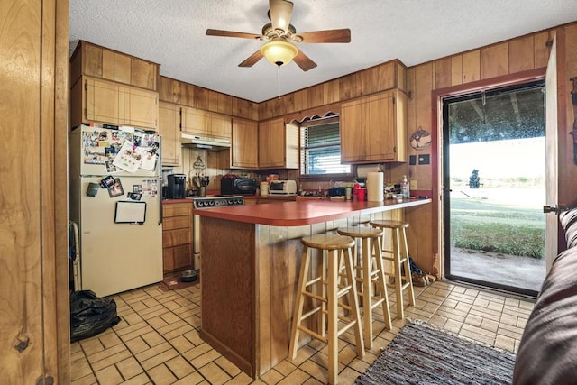 kitchen featuring ceiling fan, a kitchen breakfast bar, white refrigerator, kitchen peninsula, and range