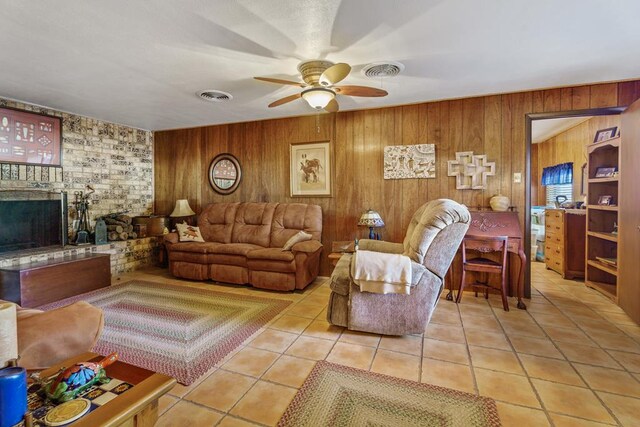 living room with ceiling fan, wood walls, light tile patterned floors, and a fireplace