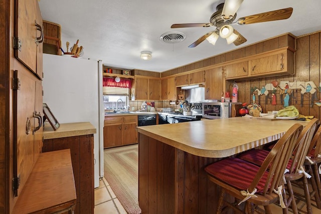 kitchen featuring sink, kitchen peninsula, wood walls, light tile patterned flooring, and appliances with stainless steel finishes