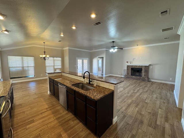 kitchen featuring a sink, light wood-style floors, open floor plan, stainless steel dishwasher, and a brick fireplace