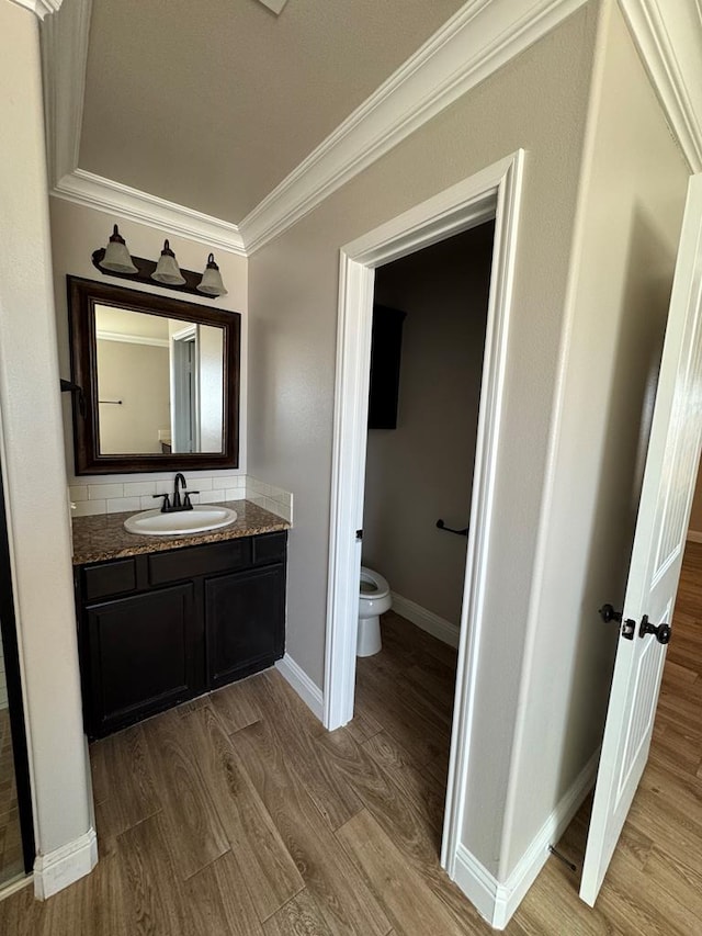 bathroom featuring toilet, ornamental molding, vanity, wood finished floors, and baseboards