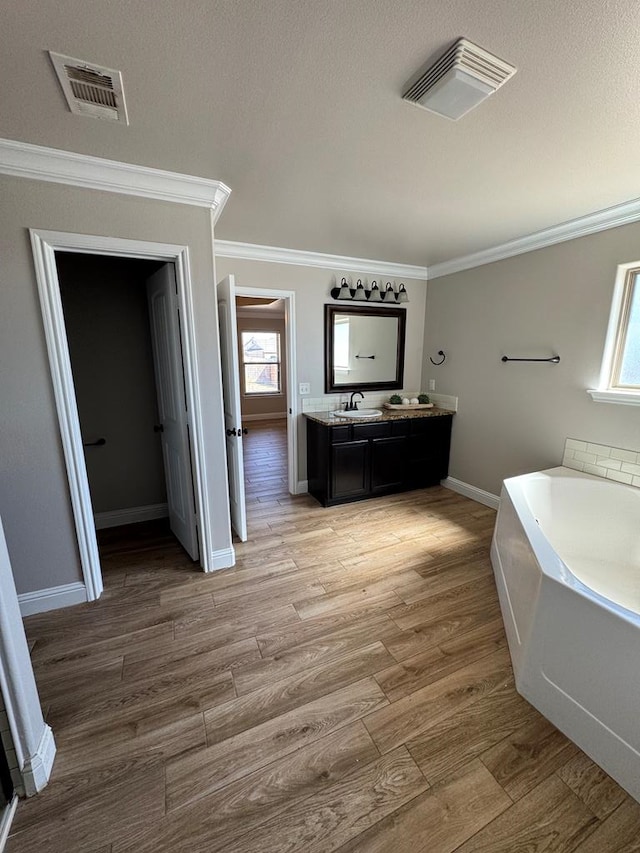 bathroom with a bath, visible vents, wood finished floors, and ornamental molding