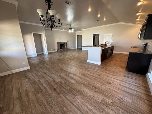 kitchen with a brick fireplace, open floor plan, a sink, vaulted ceiling, and dark stone countertops