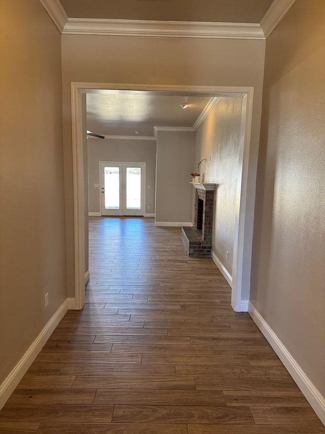 interior space with dark wood-style floors, a brick fireplace, crown molding, and baseboards