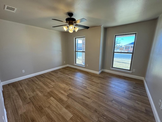 empty room with ceiling fan, wood finished floors, visible vents, and baseboards