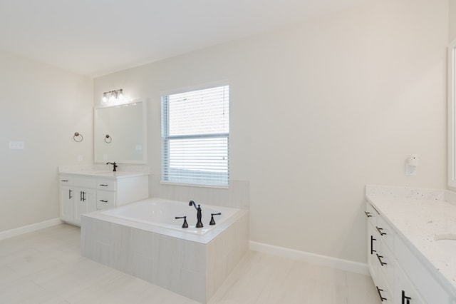 bathroom featuring a garden tub, two vanities, baseboards, and a sink