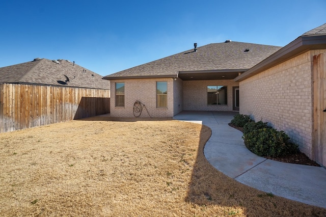 rear view of house with a patio area, brick siding, a fenced backyard, and roof with shingles