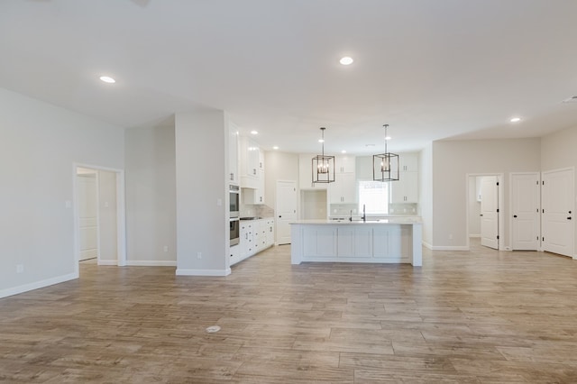 unfurnished living room with recessed lighting, baseboards, light wood finished floors, and a sink