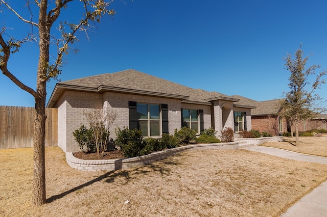 view of front of house featuring brick siding, a shingled roof, and fence