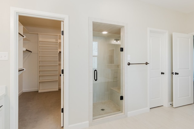 full bathroom featuring vanity, a shower stall, a spacious closet, and baseboards