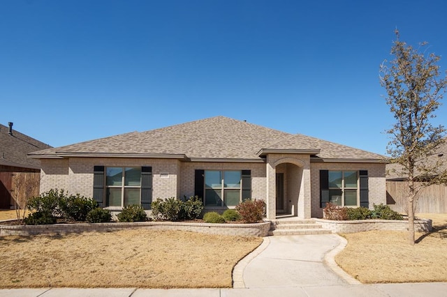 view of front of home with fence, brick siding, and a shingled roof