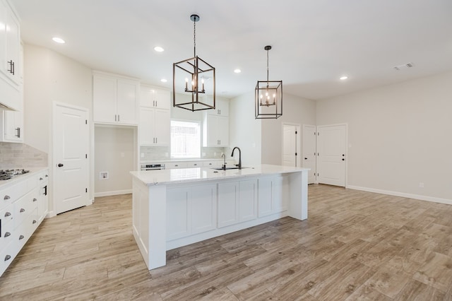 kitchen with a center island with sink, visible vents, a sink, light wood-style floors, and white cabinetry