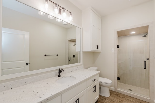 bathroom featuring wood finished floors, toilet, a stall shower, and vanity