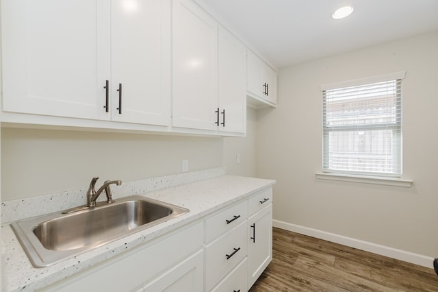 kitchen featuring baseboards, light stone counters, wood finished floors, white cabinets, and a sink