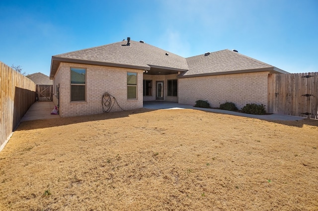 back of property with brick siding, a fenced backyard, a patio area, and roof with shingles