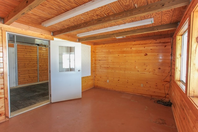 empty room featuring beam ceiling, concrete floors, and wooden walls