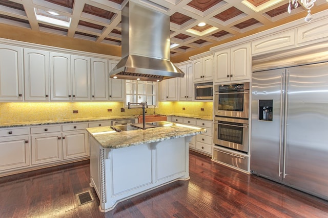 kitchen with dark wood-type flooring, coffered ceiling, white cabinets, island range hood, and stainless steel appliances