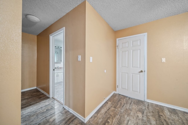 corridor with a textured ceiling, baseboards, and wood finished floors