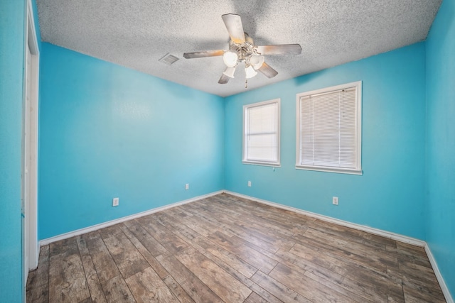 spare room featuring ceiling fan, a textured ceiling, wood finished floors, visible vents, and baseboards