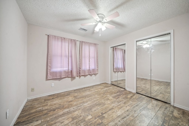 unfurnished bedroom with wood finished floors, visible vents, a textured ceiling, and two closets