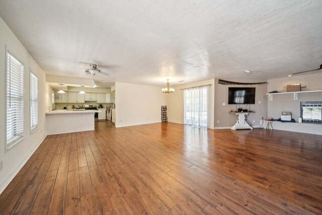 unfurnished living room featuring ceiling fan with notable chandelier, a textured ceiling, baseboards, and wood finished floors