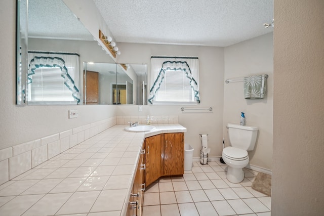 bathroom with a textured ceiling, tile patterned flooring, toilet, vanity, and baseboards