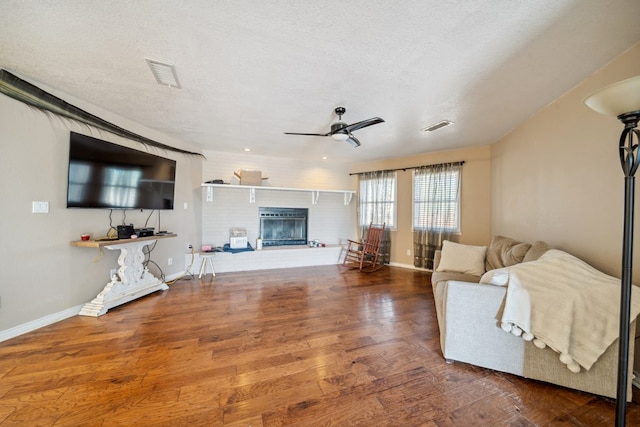 living area featuring visible vents, ceiling fan, wood finished floors, a textured ceiling, and a brick fireplace