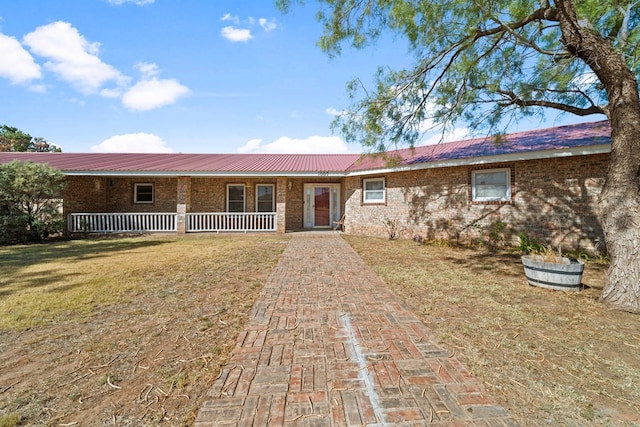 ranch-style house featuring covered porch, brick siding, metal roof, and a front yard