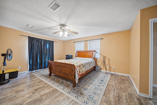 bedroom with baseboards, visible vents, a ceiling fan, wood finished floors, and a textured ceiling