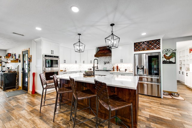 kitchen with a breakfast bar area, appliances with stainless steel finishes, custom range hood, pendant lighting, and a large island