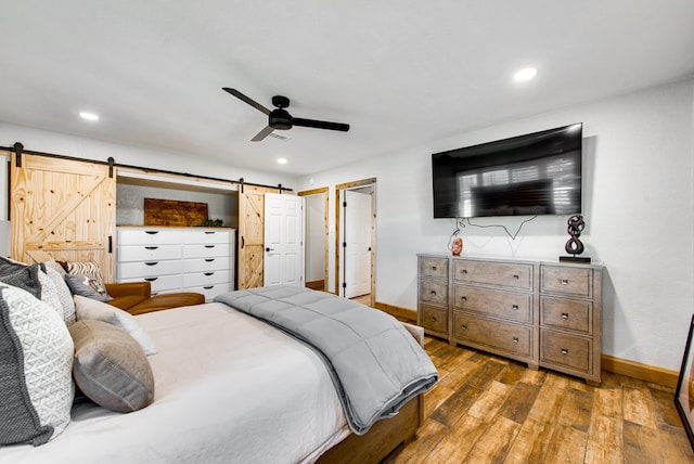 bedroom with a barn door, hardwood / wood-style floors, and ceiling fan