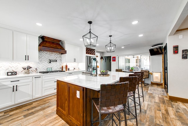 kitchen with premium range hood, a breakfast bar, an island with sink, stainless steel gas stovetop, and white cabinets