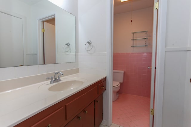 1900 Goliad St, Big Spring, TX 79720 - bathroom featuring vanity, toilet, tile patterned floors, tile walls, and wainscoting