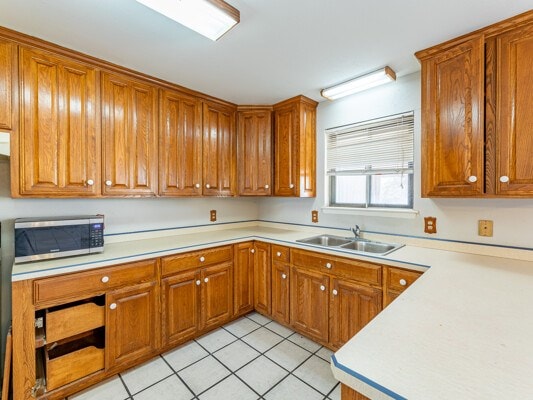 kitchen with brown cabinets, stainless steel microwave, light countertops, and a sink