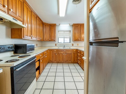 kitchen featuring light countertops, freestanding refrigerator, white electric range, and under cabinet range hood