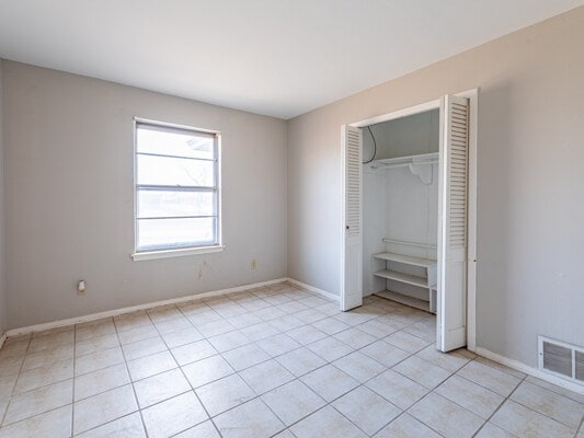 unfurnished bedroom with light tile patterned floors, a closet, visible vents, and baseboards