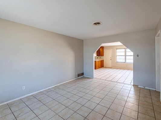 empty room featuring arched walkways, visible vents, baseboards, and light tile patterned floors